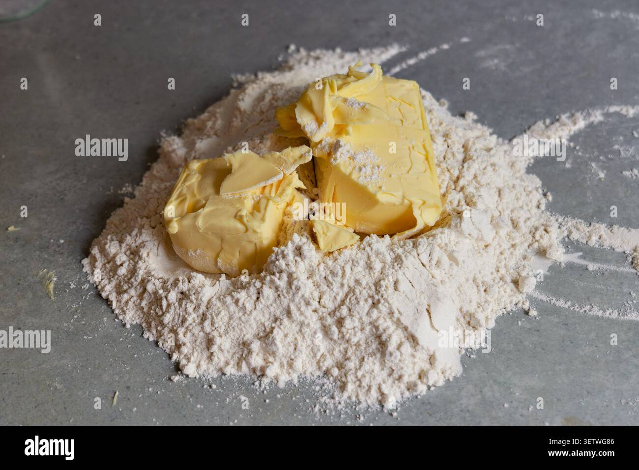 Butterstücke auf einem Haufen weißem Mehl. Nahaufnahme von frischen Butterblöcken, die auf einem Stapel Weizenmehl auf einer grauen Küchentheke platziert wurden Stockfoto