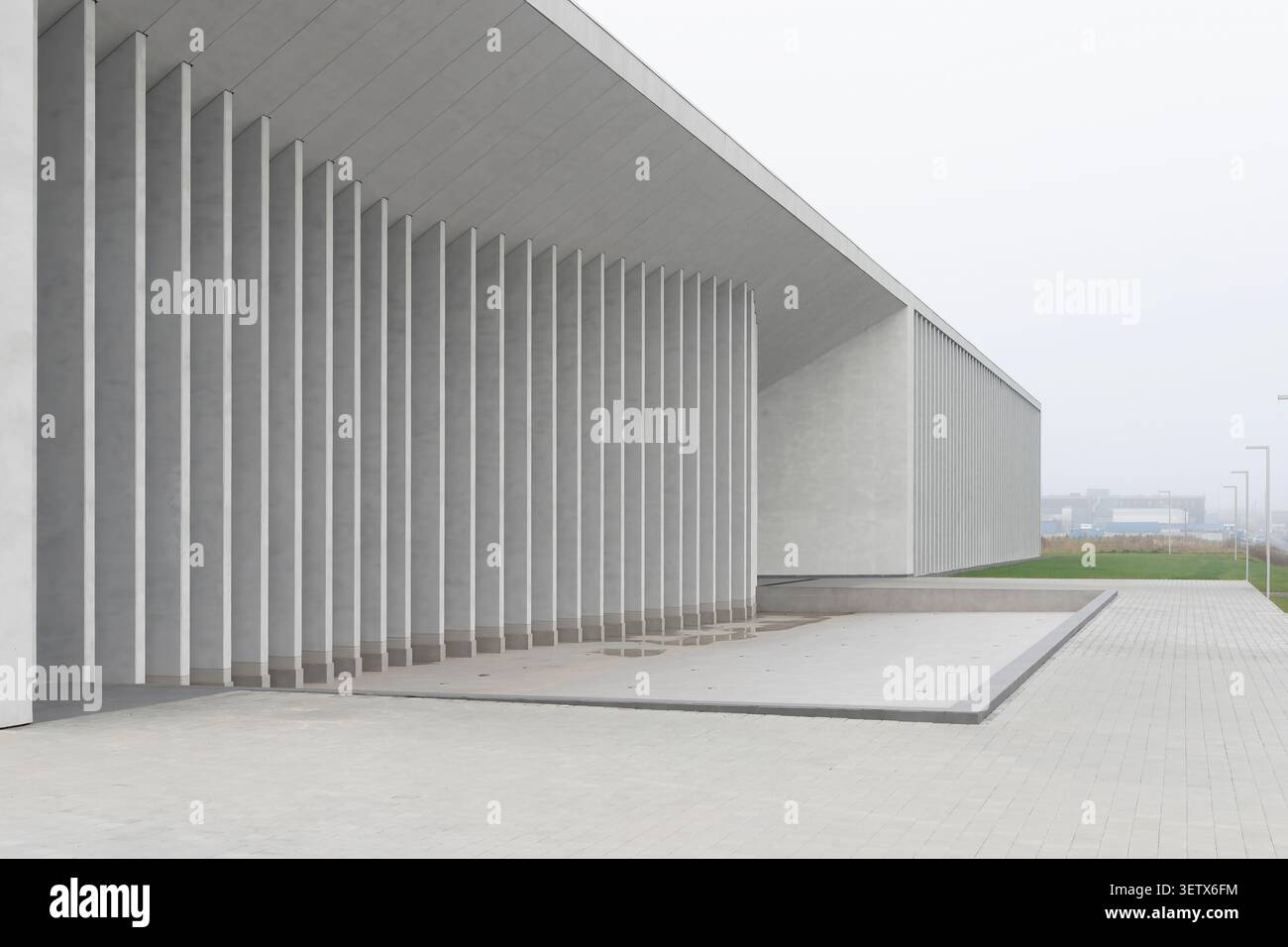 Minimalistisches Gebäude mit Betonsäulen und offenem Eingangsbereich in der Nähe von Bürgersteig. Moderne Struktur zeigt sich wiederholende Elemente und geometrische Perspektiven. Stockfoto