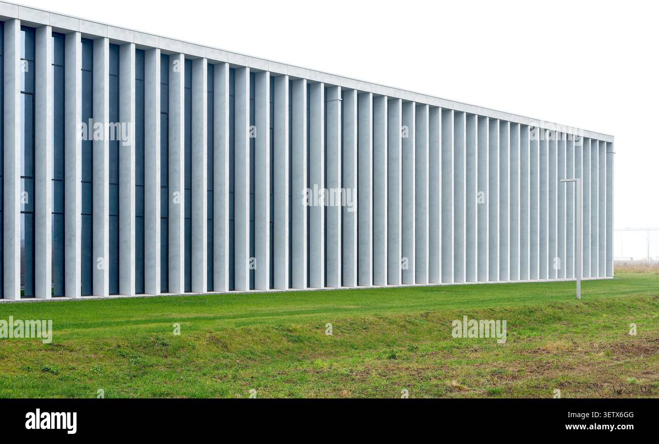 Modernes minimalistisches Gebäude mit langer Fassade und Betonsäulen in der Nähe von grünem Rasen. Lineare Struktur, die sich horizontal mit sich wiederholenden Elementen erstreckt. Konz Stockfoto