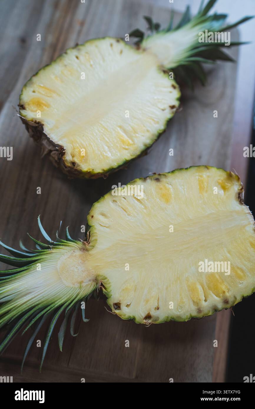 Frische Ananas, halbiert auf Holzoberfläche, zeigt gelbes Fleisch und grüne Krone Stockfoto
