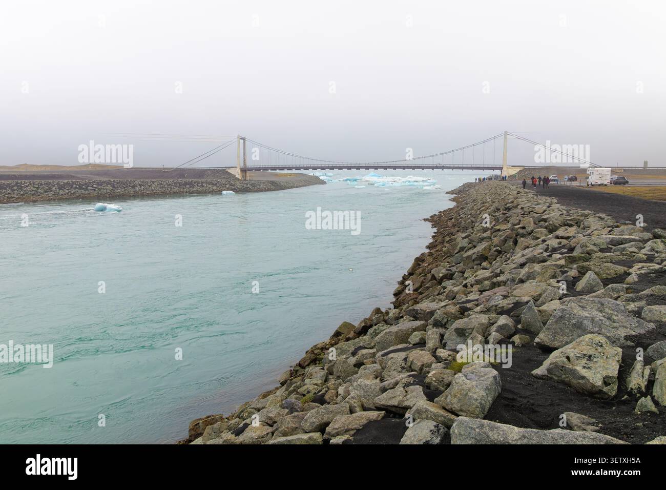 Dieses fesselnde Foto zeigt die historische Hängebrücke über den Auslasskanal, wo die Lagune von Jökulsárlón auf den Atlantischen Ozean i trifft Stockfoto