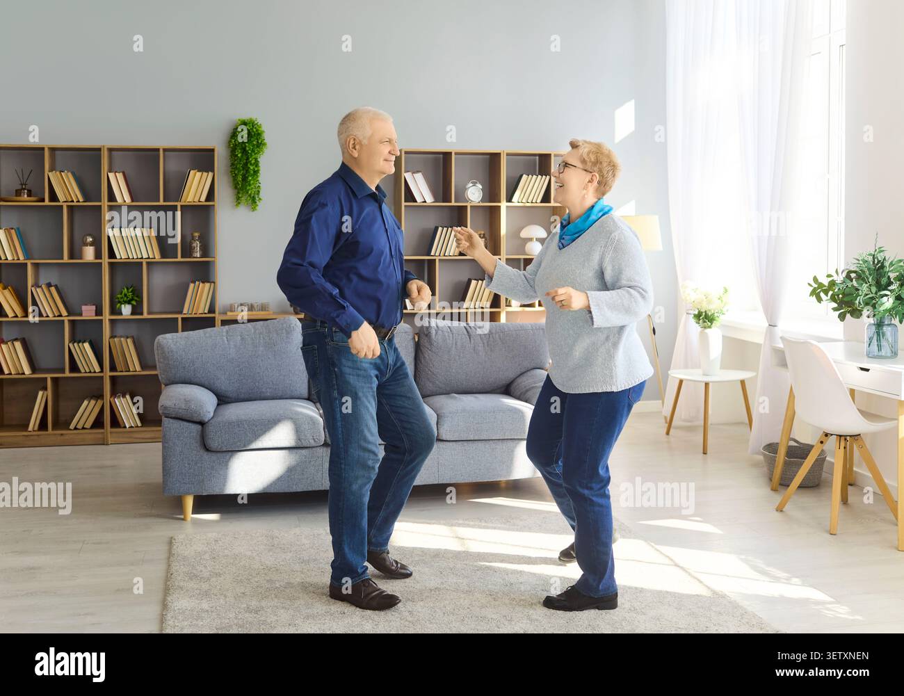 Seniorenpaar tanzt zusammen zu Hause im hellen Wohnzimmer, fröhlicher Ruhestand Stockfoto