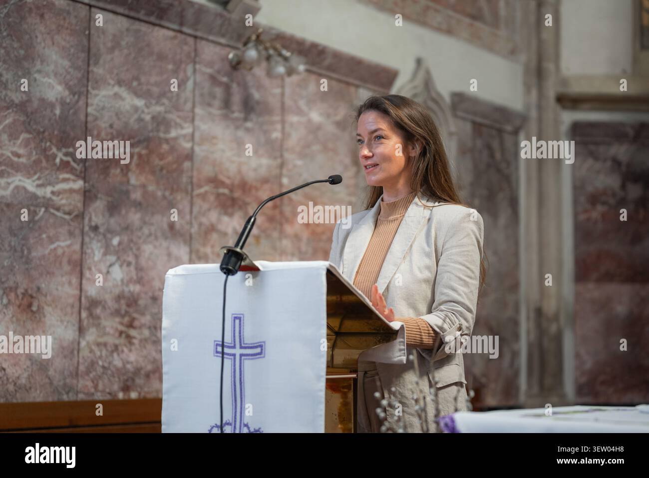 Frau in der katholischen Kirche, die hinter der Kanzel steht und die Schrift auf einem Mikrofon liest, vor der Gemeinde in der Messe. Stockfoto