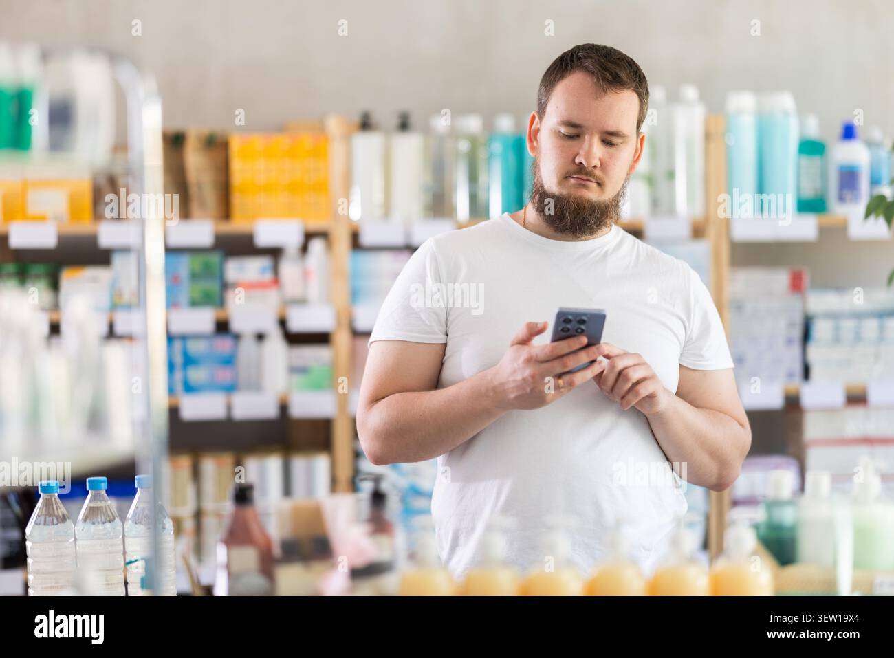 Junger Mann mit Telefon, der Medikamente und Hygieneprodukte wählt Stockfoto