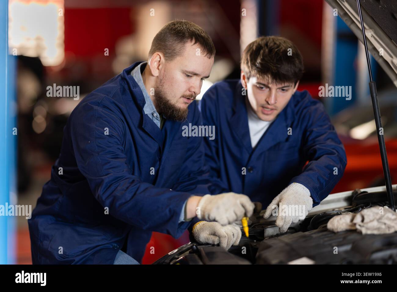 Zwei Automechaniker prüfen den Motorölstand unter der Motorhaube zusammen in der Garage Stockfoto