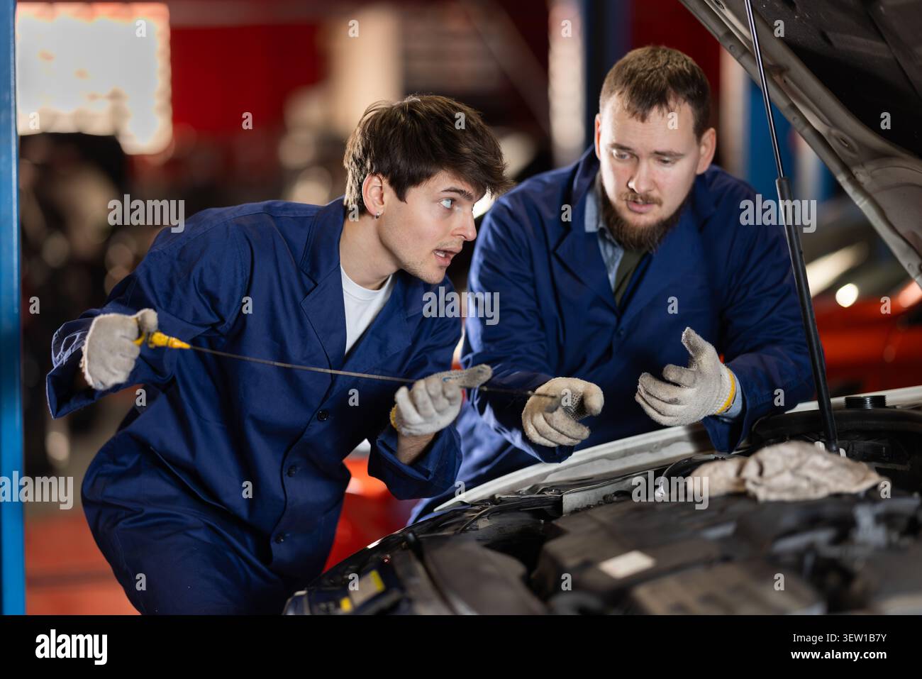 Zwei Automechaniker prüfen den Motorölstand unter der Motorhaube zusammen in der Garage Stockfoto