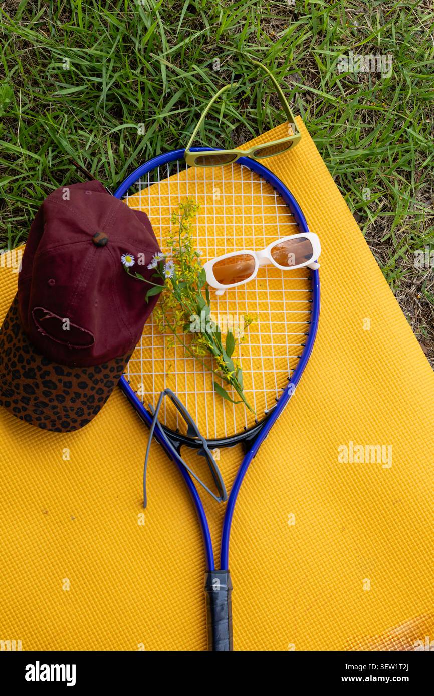 Flache Aufstellung von Tennisschläger, Sonnenbrille und Cap auf Yoga Matte im Freien Stockfoto