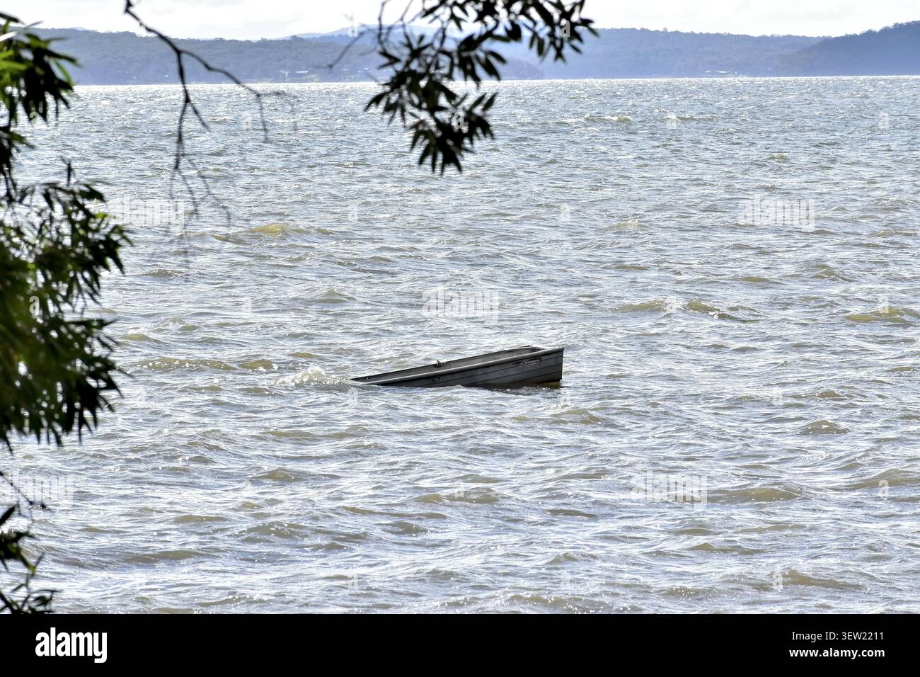 Ein gekipptes, teilweise versunkenes Boot liegt tief im fließenden Wasser. Stockfoto