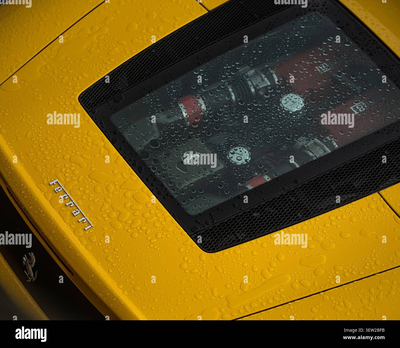 Nahaufnahme der Motorraumabdeckung eines knallgelben Ferrari-Supersportwagens im Regen. Stockfoto