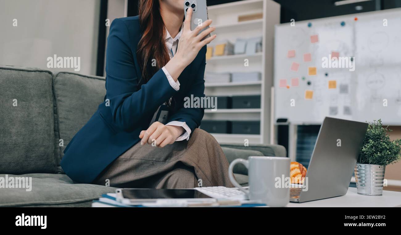 Junge asiatische Geschäftsfrau, die am Telefon telefoniert und bei der Arbeit ein digitales Tablet verwendet Stockfoto