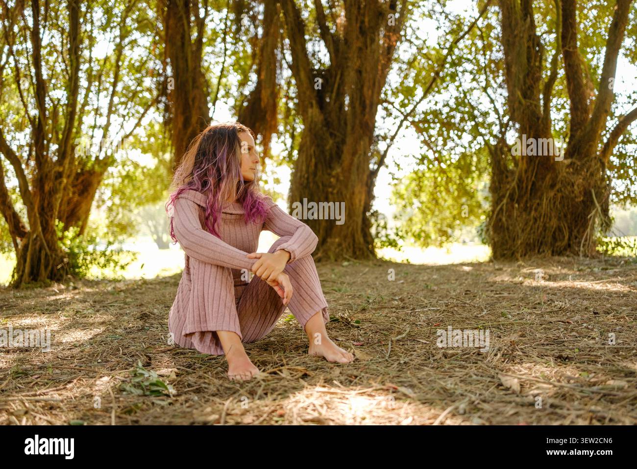 Frau, die barfuß auf dem Boden sitzt und friedlich in einer Waldlandschaft reflektiert Stockfoto