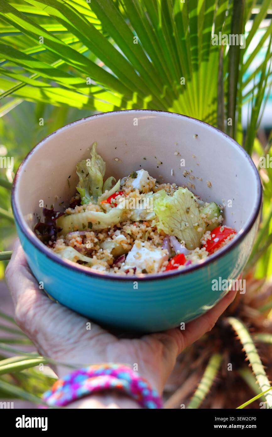 Frischer mediterraner Couscous-Salat mit Feta-Käse in der Schüssel im Freien inmitten tropischer Vegetation Stockfoto