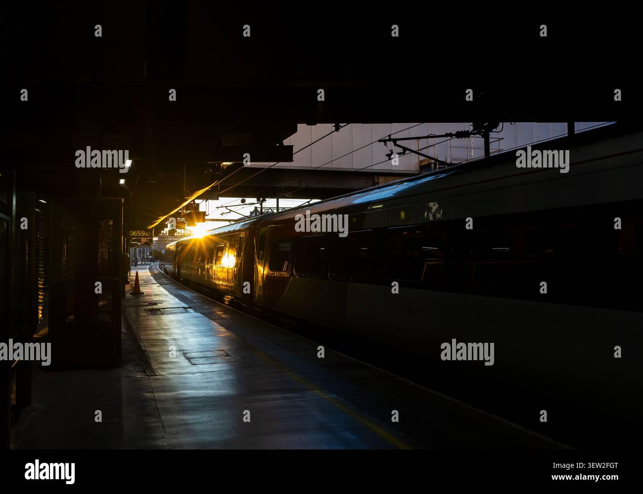 Fahren Sie an einem Bahnsteig im Bahnhof Leeds mit einem Lichtstoß von niedrigem goldenem Licht am anderen Ende einer dunklen verlassenen Halle Stockfoto