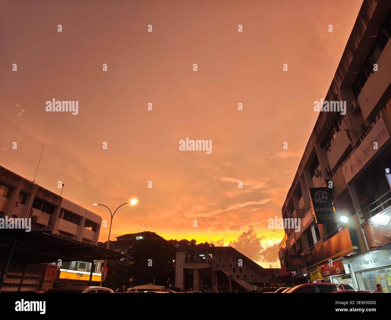 Ladenhäuser und lokale Geschäftsgebäude wurden vor einem intensiven, lebhaften orangefarbenen Sonnenuntergang in einem urbanen Gebiet eingerahmt. Ideal für Hintergrundbilder und Hintergrundbilder. Stockfoto
