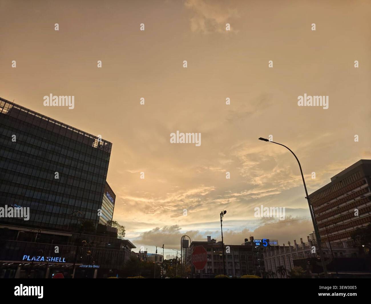 Große Geschäftsgebäude flankieren die weite Perspektive eines blassgoldenen Abendhimmels. Ideal für Hintergrundbilder und Hintergrundbilder. Stockfoto