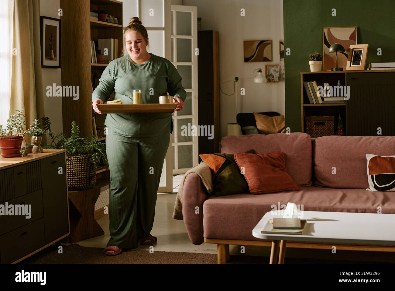 Frau in Übergröße, die ein Frühstückstablett zu Hause für die Lifestyle-Kampagne trägt Stockfoto