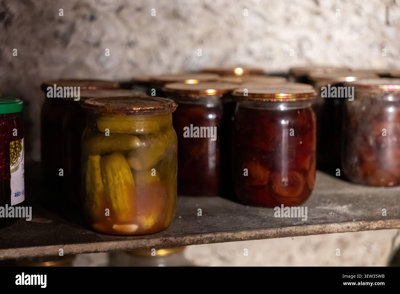 Reihen von Vintage-Glasbehältern mit fermentiertem Gemüse und konserviertem Obst, die auf einem Holzregal in einem Steinkeller gelagert sind und Gefühle von se wecken Stockfoto
