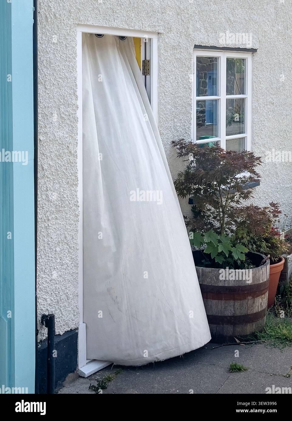 In der Hitzewelle von 2026 benutzen die Bewohner eines nach Süden gerichteten Hauses einen weißen Vorhang vor ihrer Haustür, um das Sonnenlicht zu reflektieren und warme Luft fernzuhalten Stockfoto