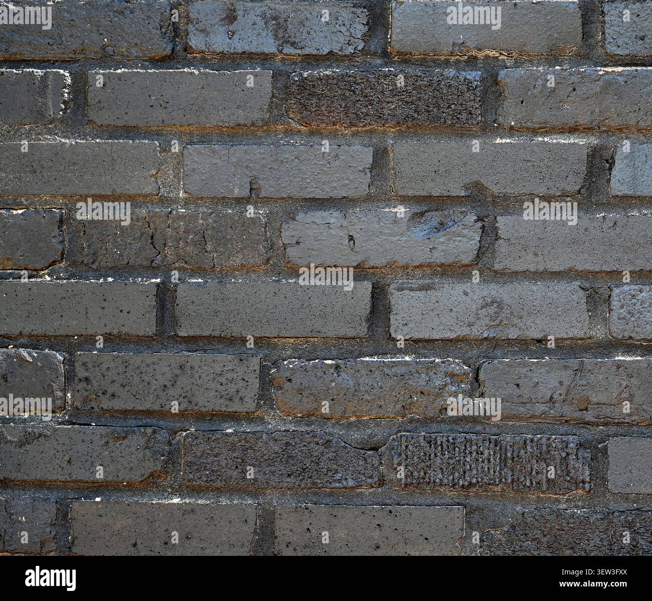Schwarz lackierte, zurückgewonnene Ziegelwand mit glatten und rauen Ziegeln, abgebrochene Farbe, die darunter liegenden Ziegel und Mörtel freigibt Stockfoto
