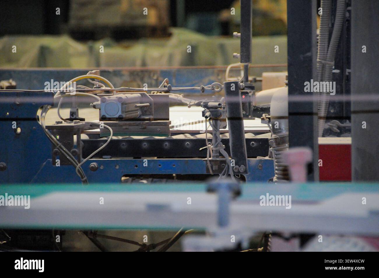 Detaillierte Ansicht mechanischer Komponenten und Sensoren auf einem Fördersystem, das Keramikfliesen durch einen automatisierten industriellen Prozess transportiert. Stockfoto