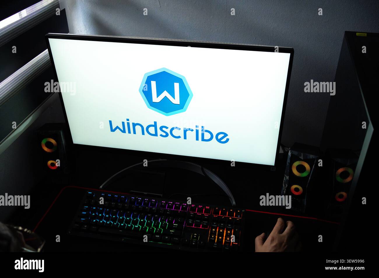 Eine Person an einem Schreibtisch mit dem Windscribe VPN- und Digital-Privacy-Logo, das auf einem Computermonitor angezeigt wird Stockfoto
