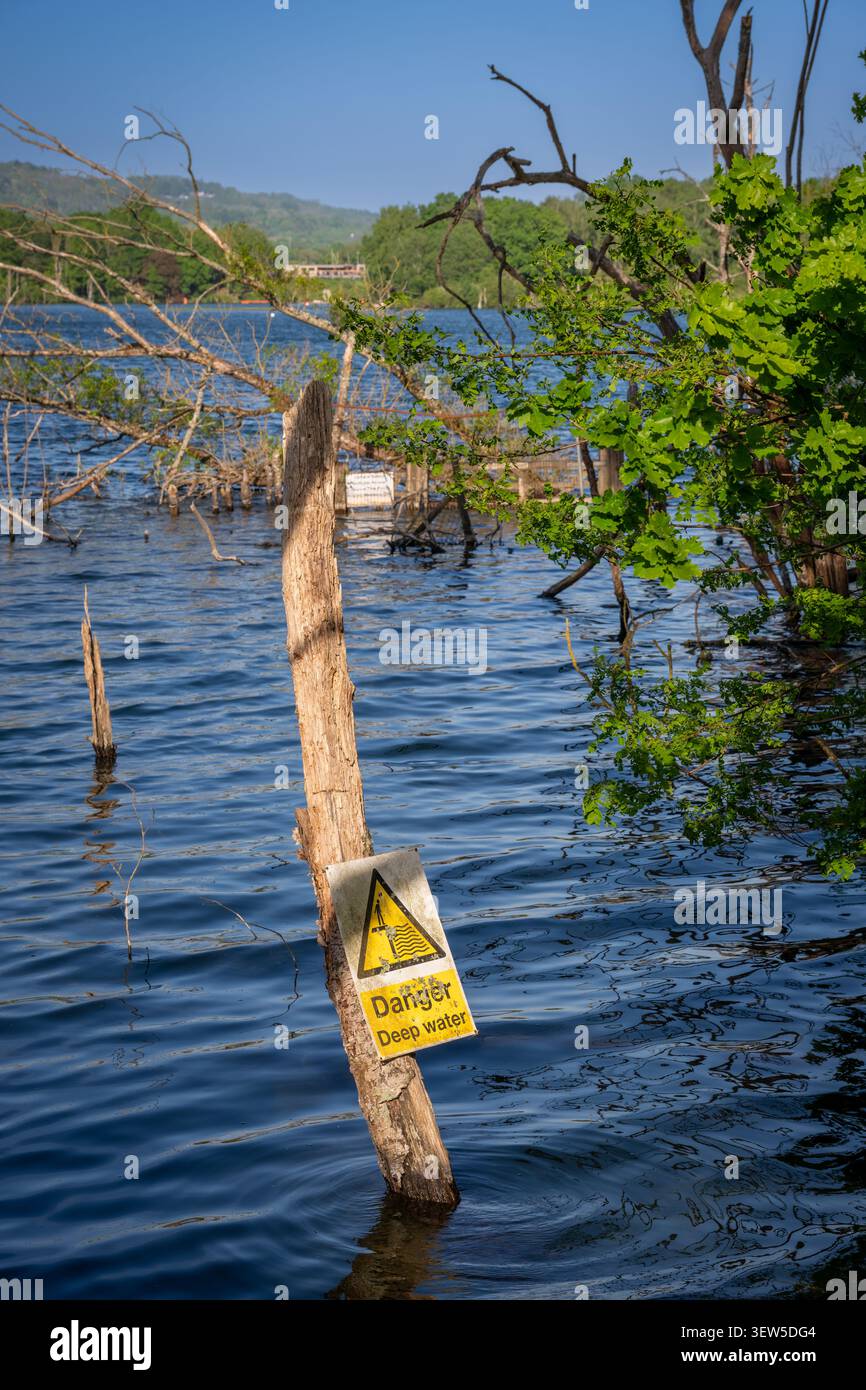 Mercers Lake in der Nähe von Merstham, Surrey, Großbritannien, mit Bäumen an einem Sommertag. Ein Gefahrenzeichen warnt vor tiefem Wasser. Stockfoto