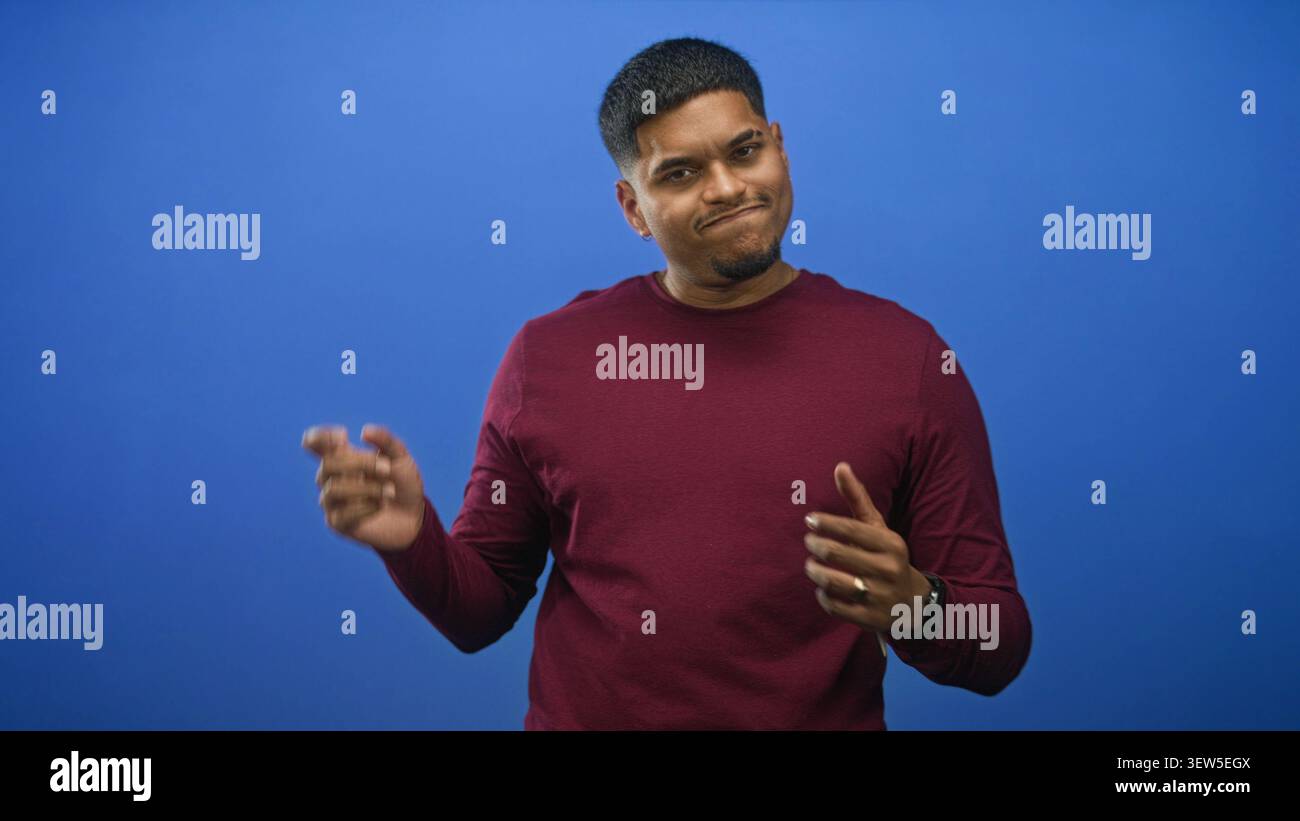 In einem blauen Studio mit kastanienbraunem Pullover und Armbanduhr, Handflächen sichtbar und Augen geschlossen; mildes Vergnügen. Stockfoto