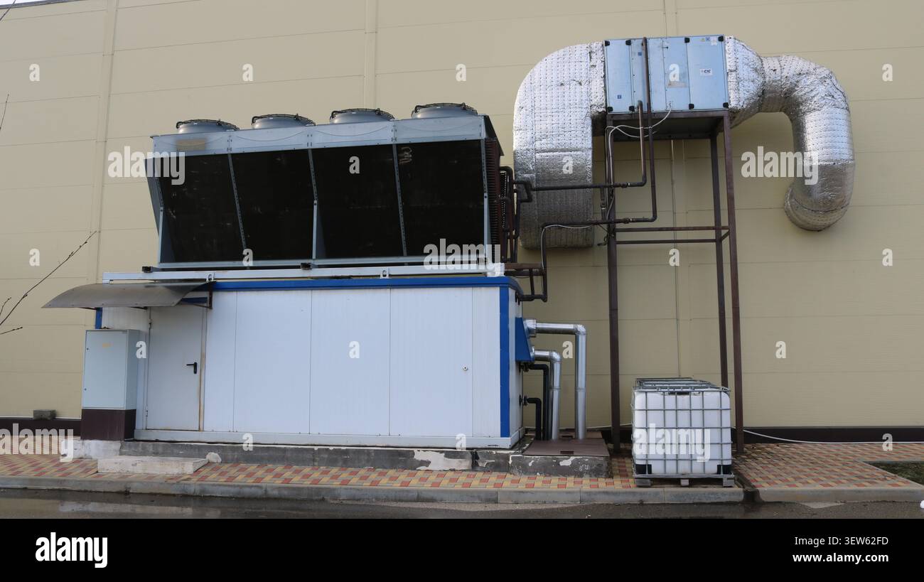 An der Gebäudewand ist ein Industriekühler mit einem abgesetzten Kondensator installiert. Das System umfasst isolierte Luftkanäle und Kühlgebläse Stockfoto