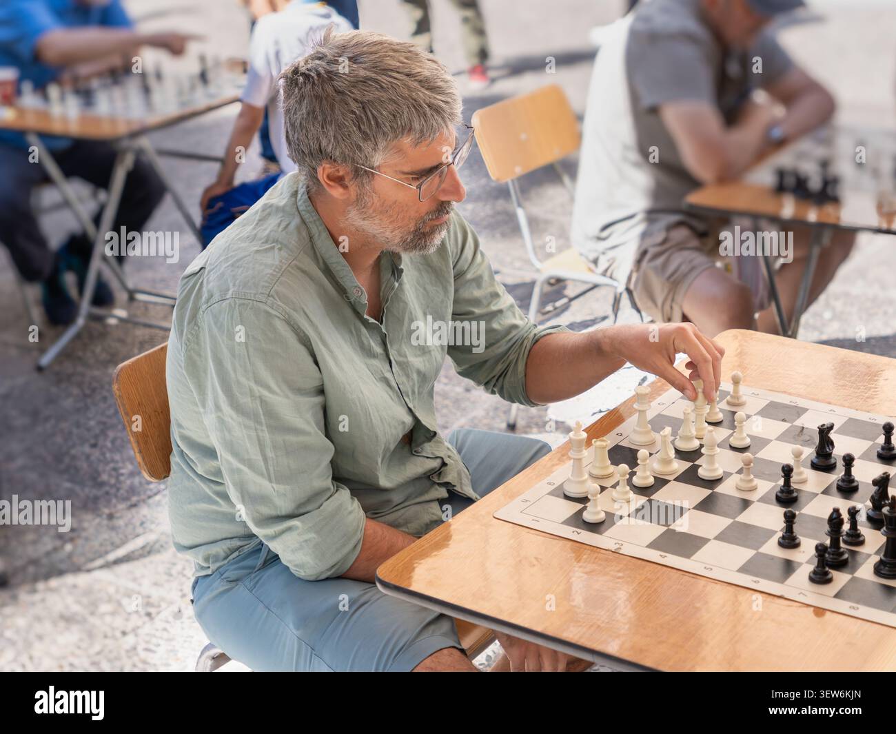 Ein Mann bewegt ein weißes Stück auf einem Schachbrett, konzentriert sich auf das Spiel während eines Treffens im Freien. Intellektuelle Herausforderung und Freizeitkonzept Stockfoto