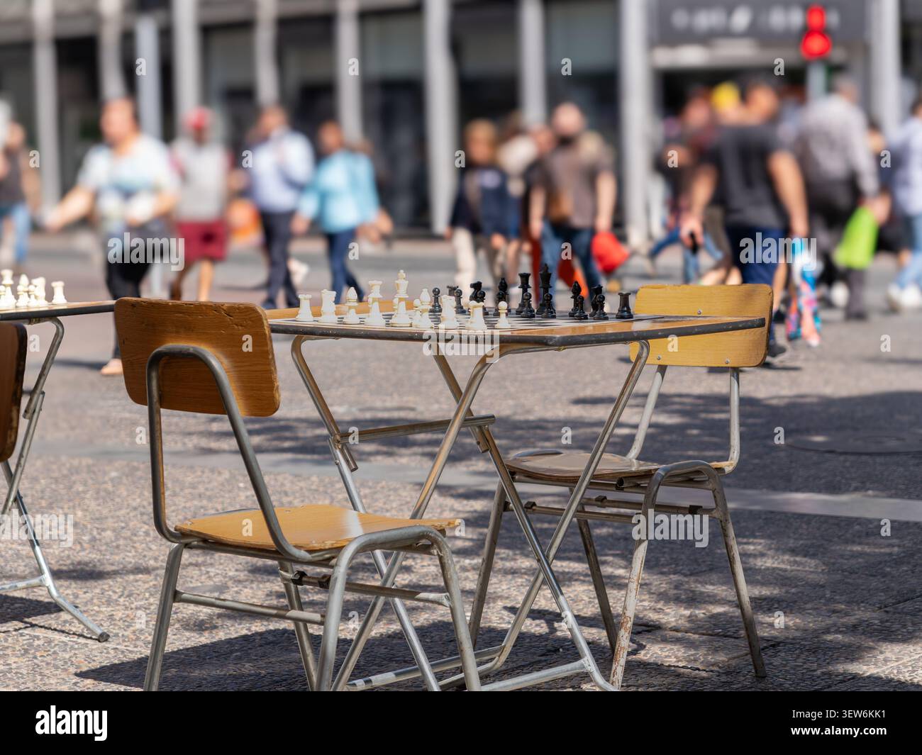 Das Schachbrett wartet auf Spieler in einer städtischen Straße mit Stühlen und unscharfen Menschen, die im Hintergrund laufen Stockfoto
