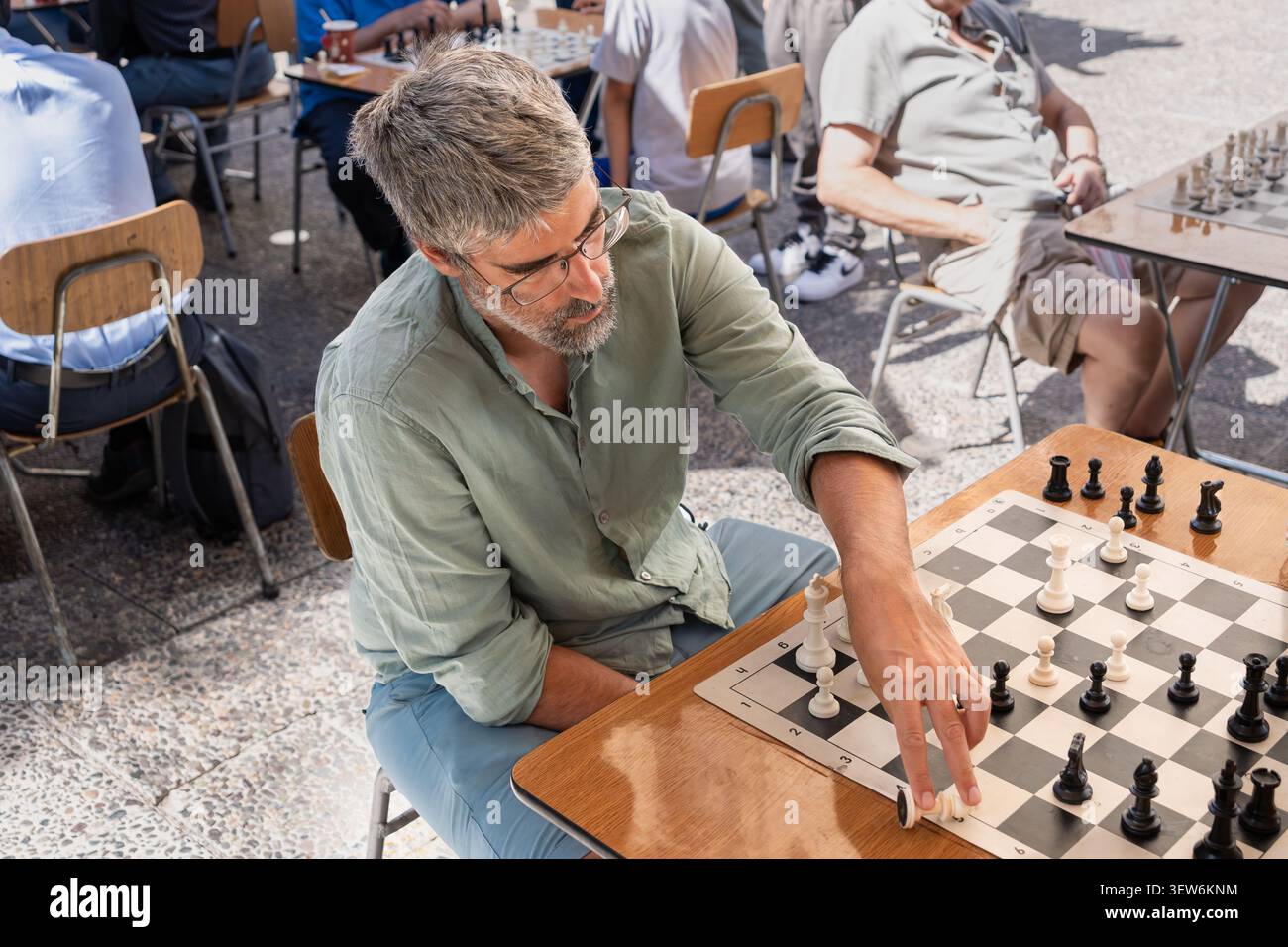 Ein Mann bewegt ein Schachstück, beteiligt sich an einem strategischen Brettspiel. Spieler, die sich auf intellektuelle Herausforderungen und Freizeitaktivitäten konzentrieren Stockfoto