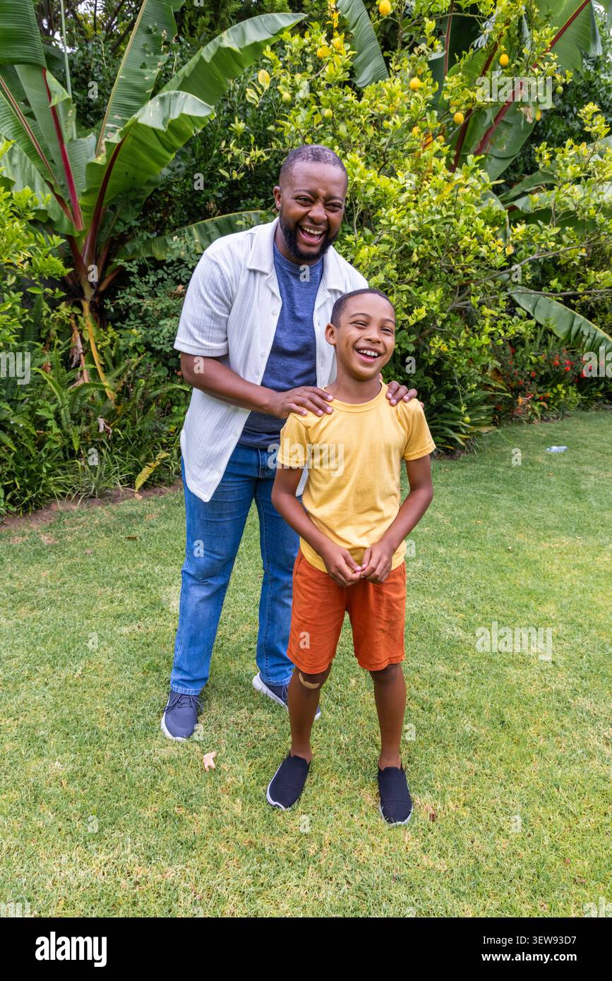 Afroamerikanischer Vater und Sohn stehen und lachen auf gepflegtem Rasen mit Zitrusbaum Stockfoto