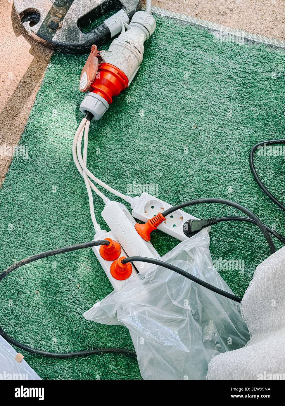 Industrielle elektrische Verlängerungskabel, Steckdosenleisten und Hochleistungssteckverbinder, die auf Kunstrasen an einer Außenarbeitsstätte angeordnet sind. Praktisches Bild für Stockfoto