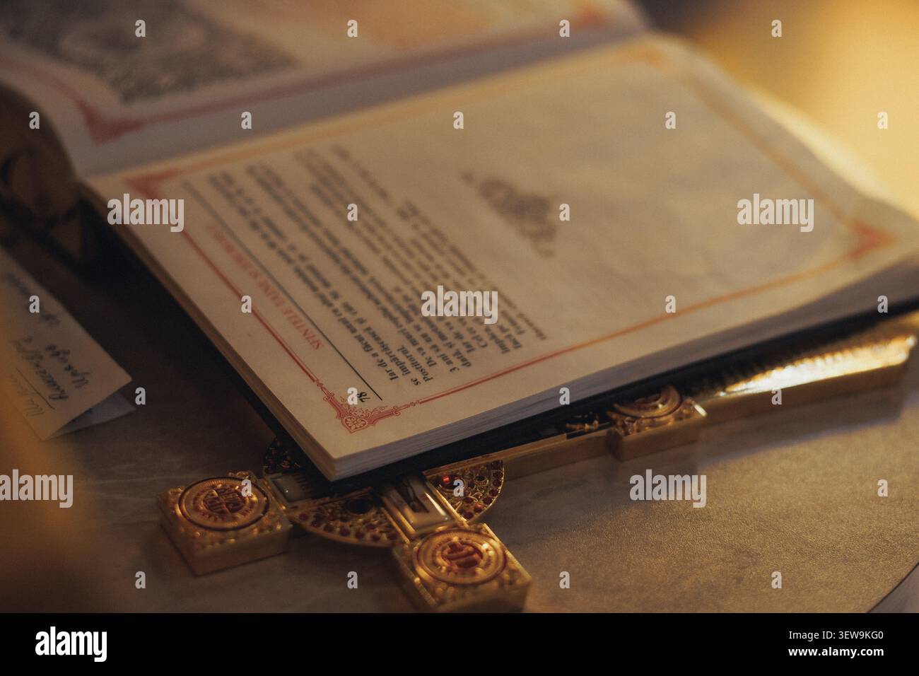 Warmes Licht leuchtet sanft über dem alten Buch. Das goldene Kreuz ruht neben offenen Seiten, Ehrfurcht. Schriftzeilen bilden heilige, feierliche Linien. Verblasste Abdeckung Stockfoto