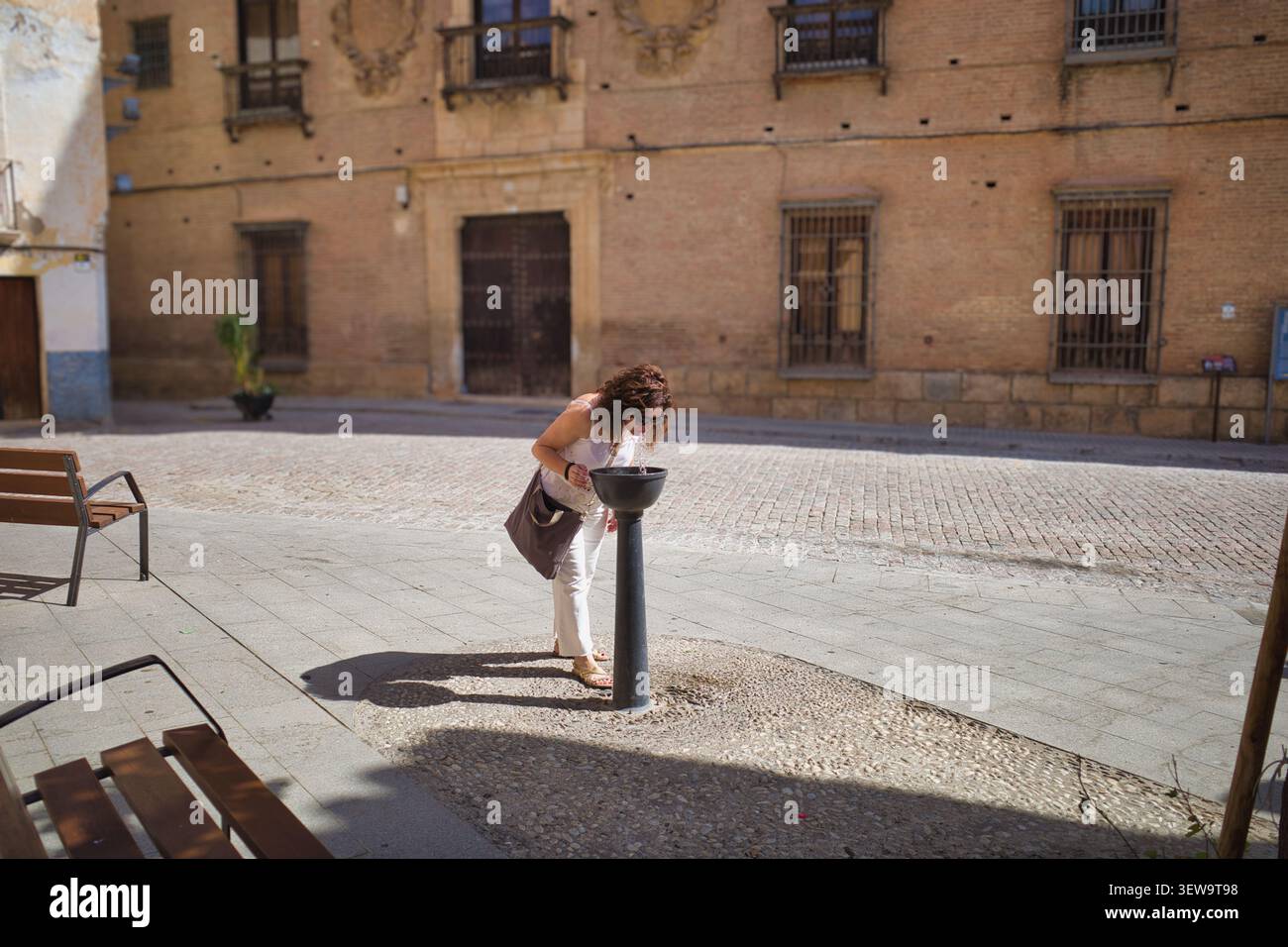 Frau trinkt aus einem öffentlichen Brunnen auf einem Stadtplatz Stockfoto