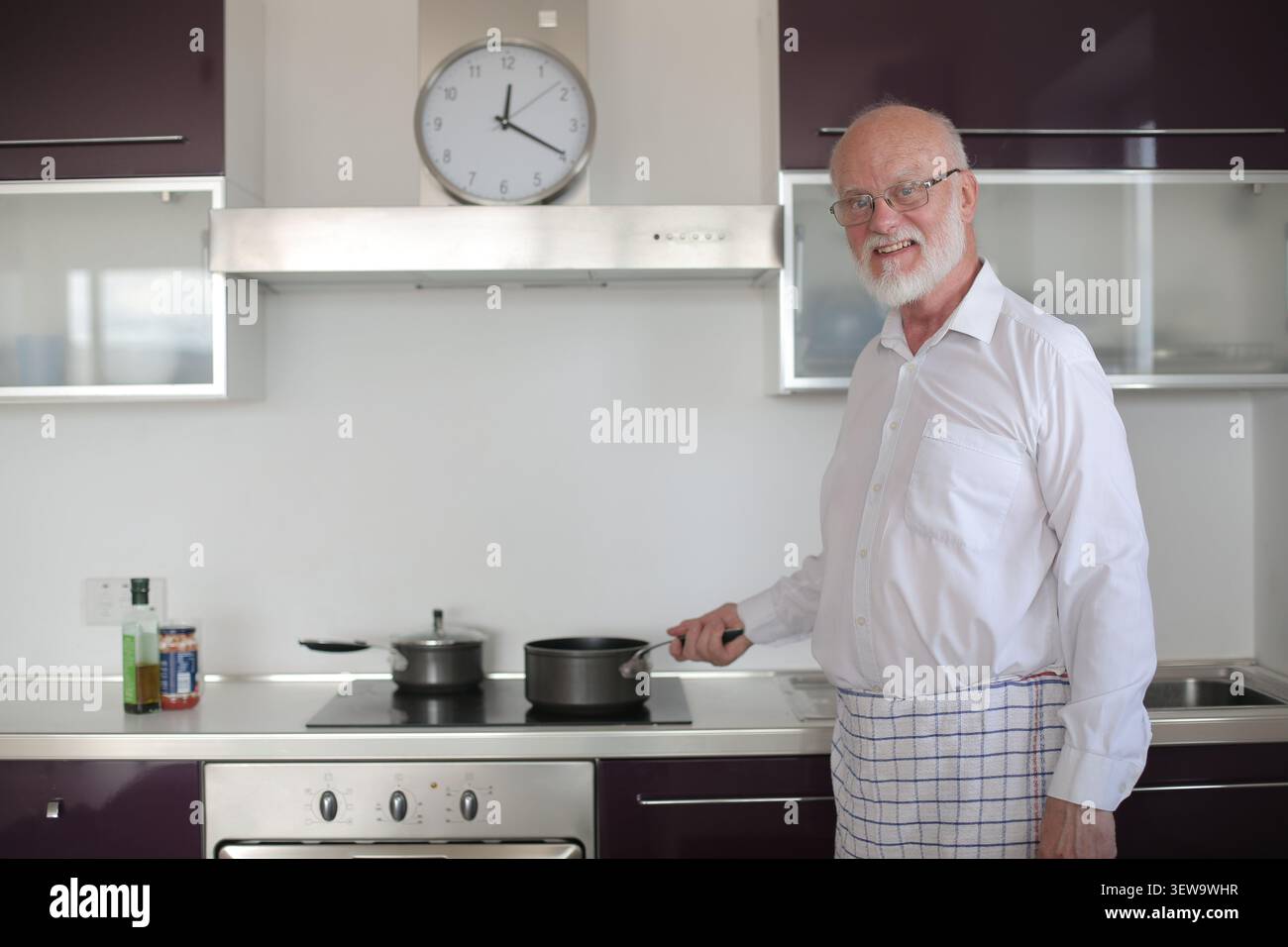 Glücklicher Senior-Mann, der in seiner modernen Küche kocht Stockfoto