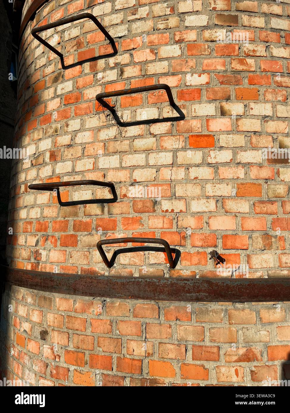 Nahaufnahme einer gekrümmten alten Ziegelkaminoberfläche mit eisernen Leitersprossen und horizontalem Metallband Stockfoto