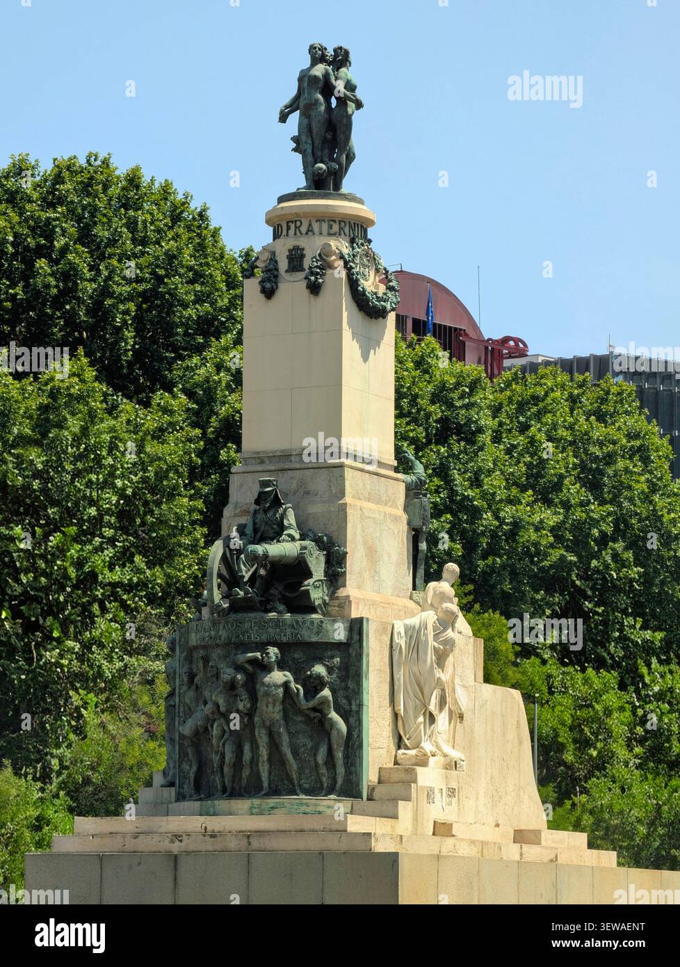 Eine Aufnahme eines hohen, mehrstufigen Stein- und Bronzemonuments mit komplizierten Skulpturen und Reliefs vor dem Hintergrund üppig grüner tr - Smartphone-aufgenommenes Stockfoto