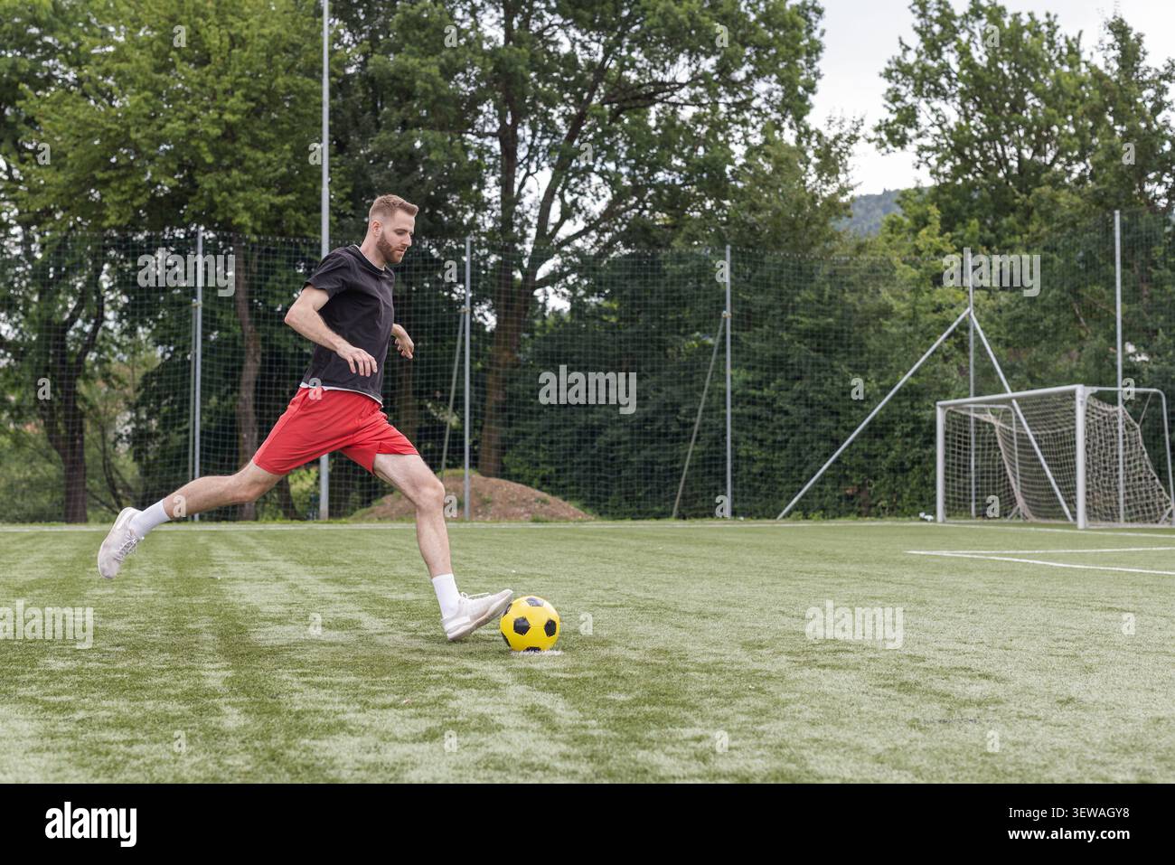 Ein männlicher Fußballspieler übt während eines Trainings auf einem von Bäumen umgebenen Freigelände Dribbling- und Schießfähigkeiten aus. Stockfoto