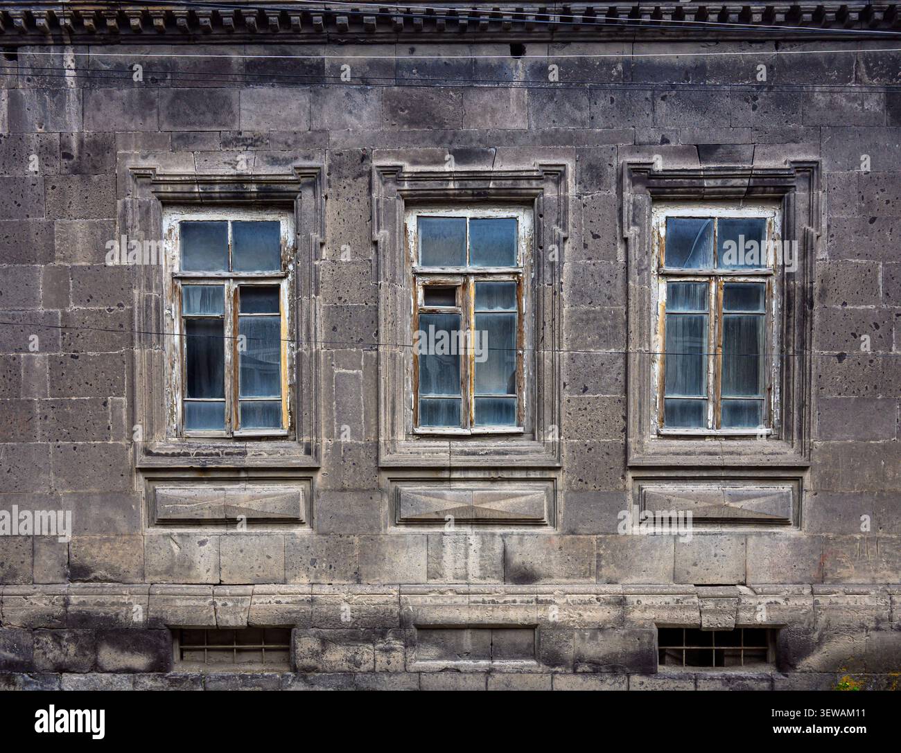 Verwittertes Steingebäude mit drei Fenstern. Die Fenster zeigen gebrochene Scheiben und abblätternde Farbe Stockfoto