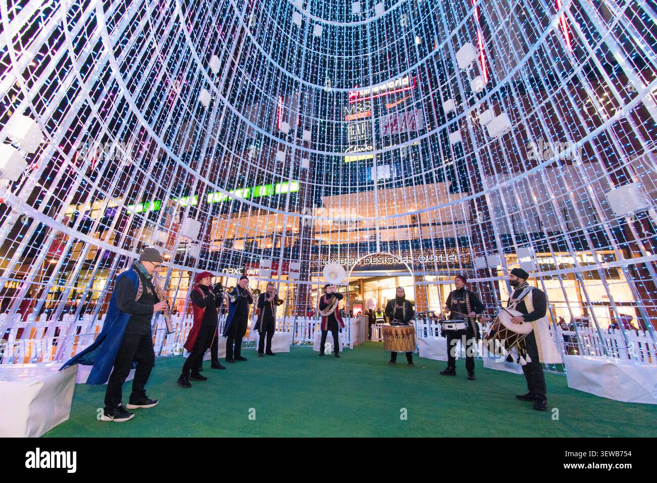 Eine Blaskapelle tritt in der riesigen Lichtinstallation im Londoner Designer Outlet in Wembley auf und sorgt für festlichen Beifall auf dem Platz. Stockfoto