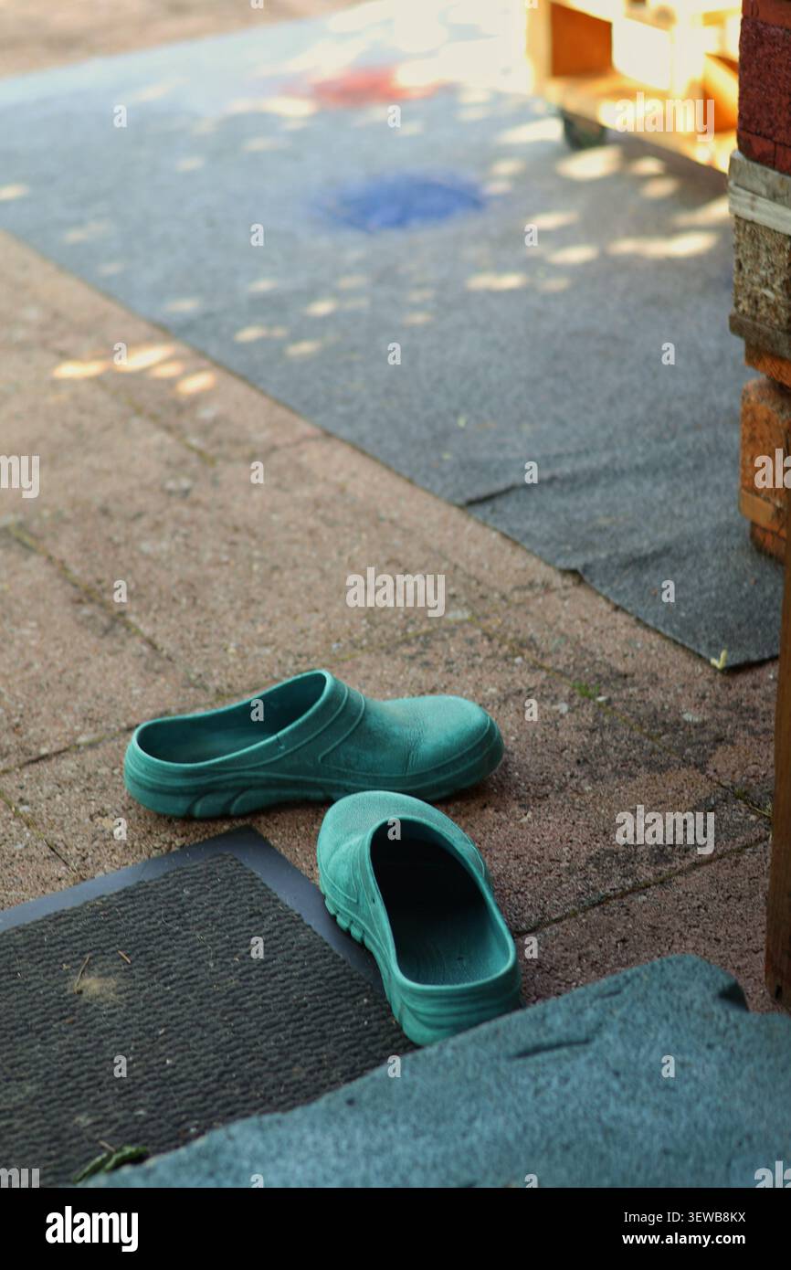 Grüne Gartenclogs am Terrasseneingang in rustikaler Outdoor Home Setting Stockfoto