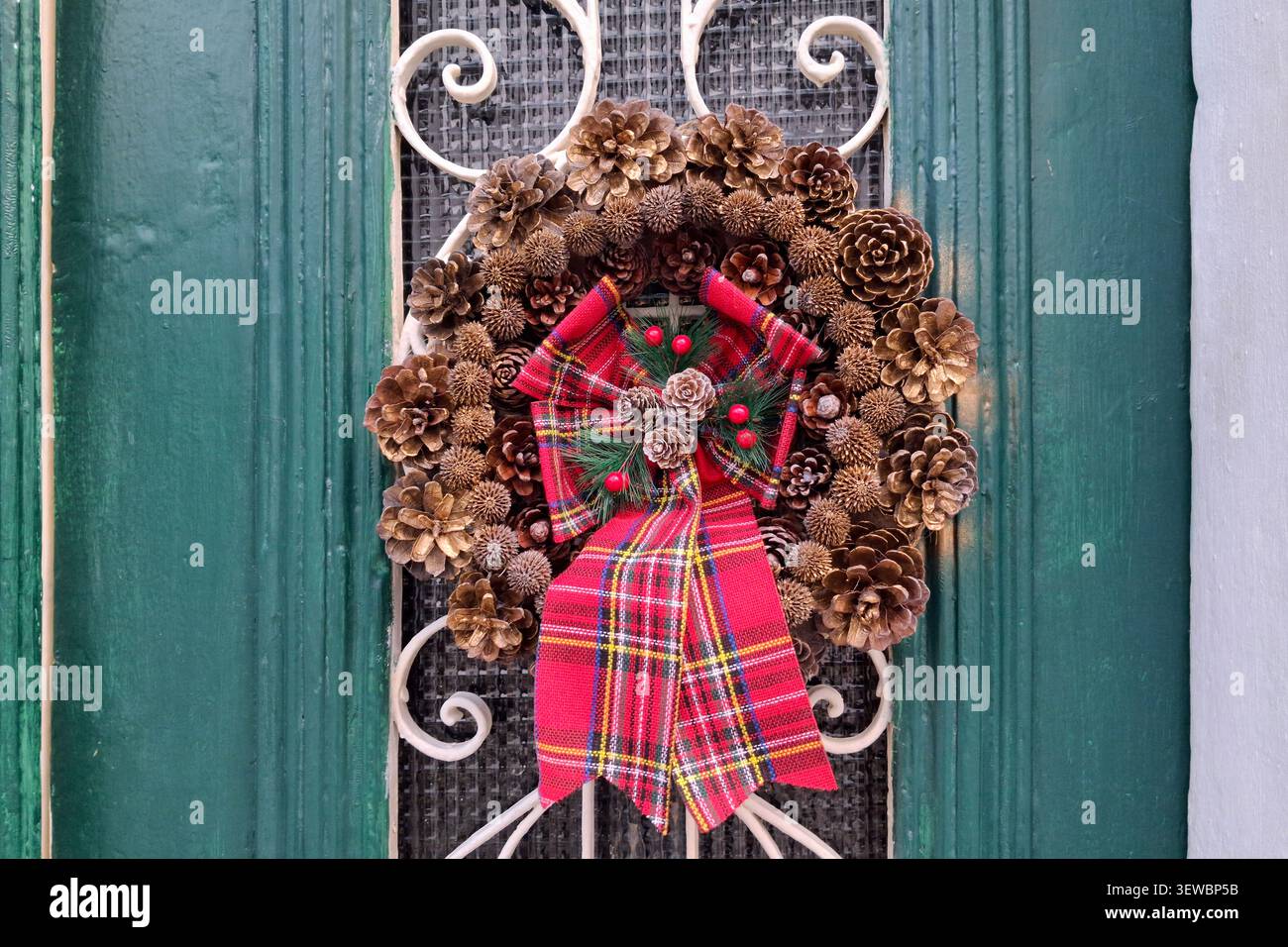 Weihnachtskranz aus Tannenzapfen mit einem großen roten Band, an der Haustür eines Hauses. Stockfoto