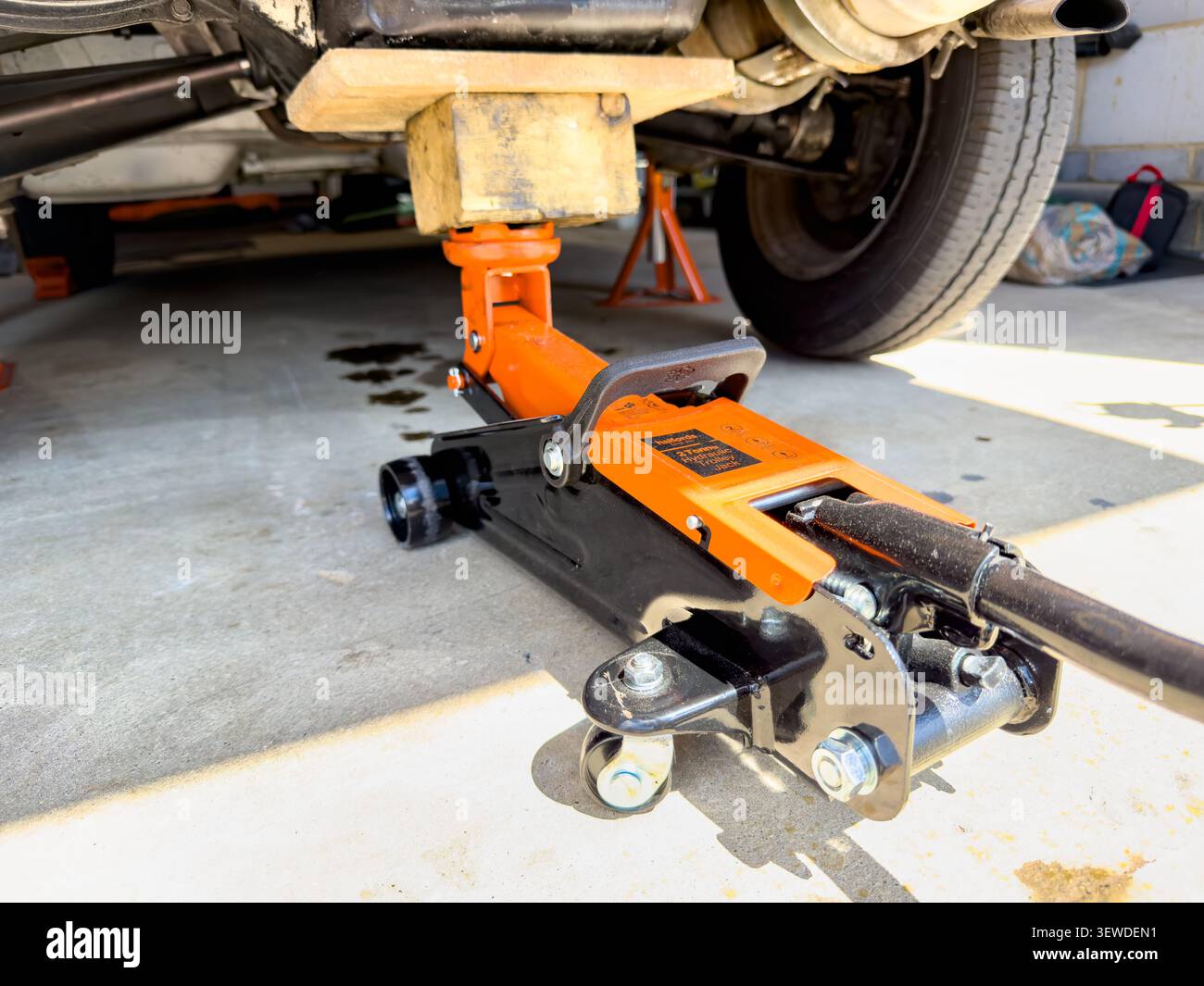 Orangefarbener und schwarzer hydraulischer Wagenheber zum Anheben eines Fahrzeugs auf einer Betonauffahrt für Reparatur und Wartung Stockfoto