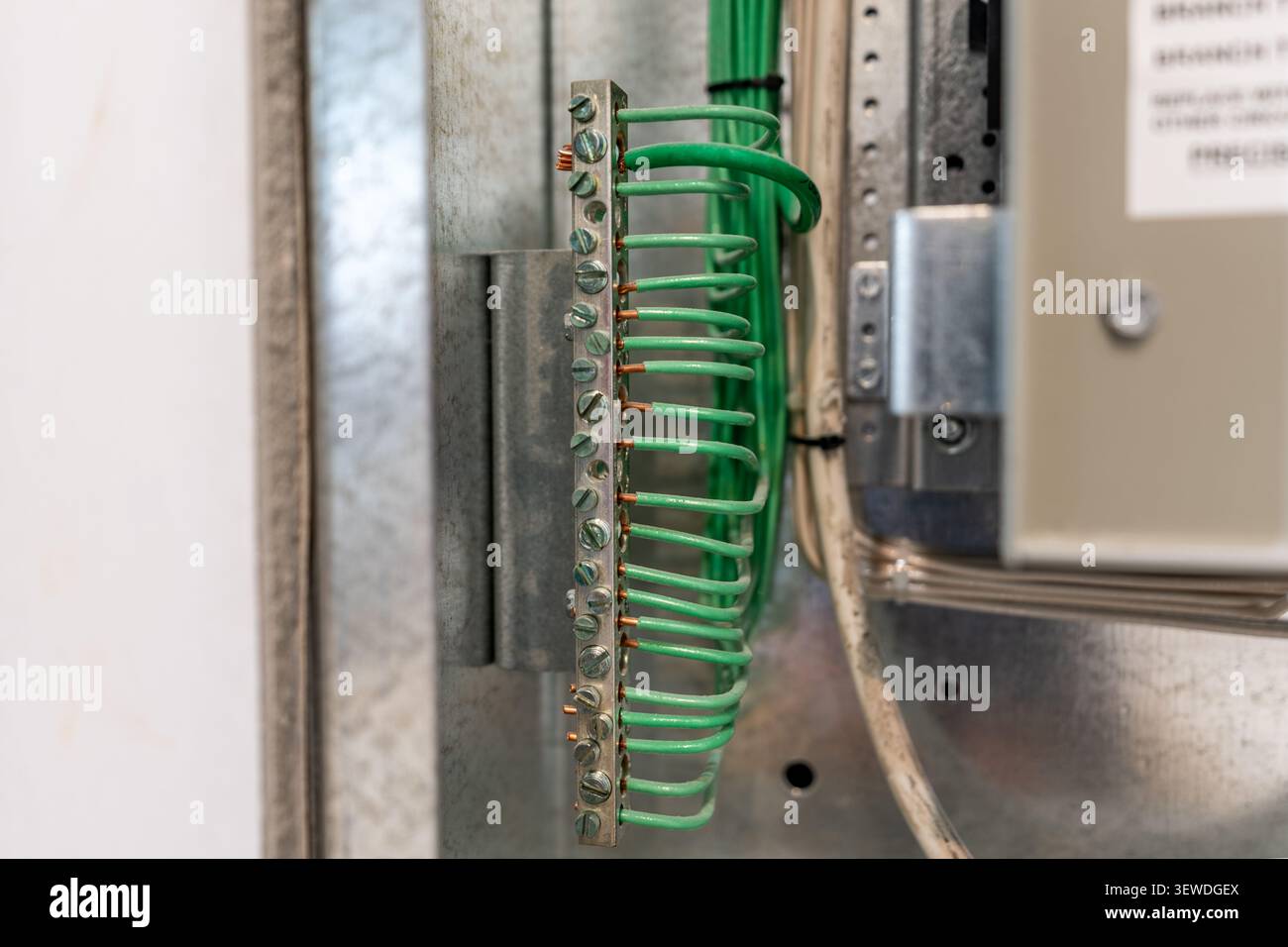Foto einer geerdeten elektrischen Sammelschiene in einer Wartungsplatte aus Metall, mit mehreren grünen isolierten Drähten, die sicher mit Klemmenschrauben verbunden sind. Stockfoto