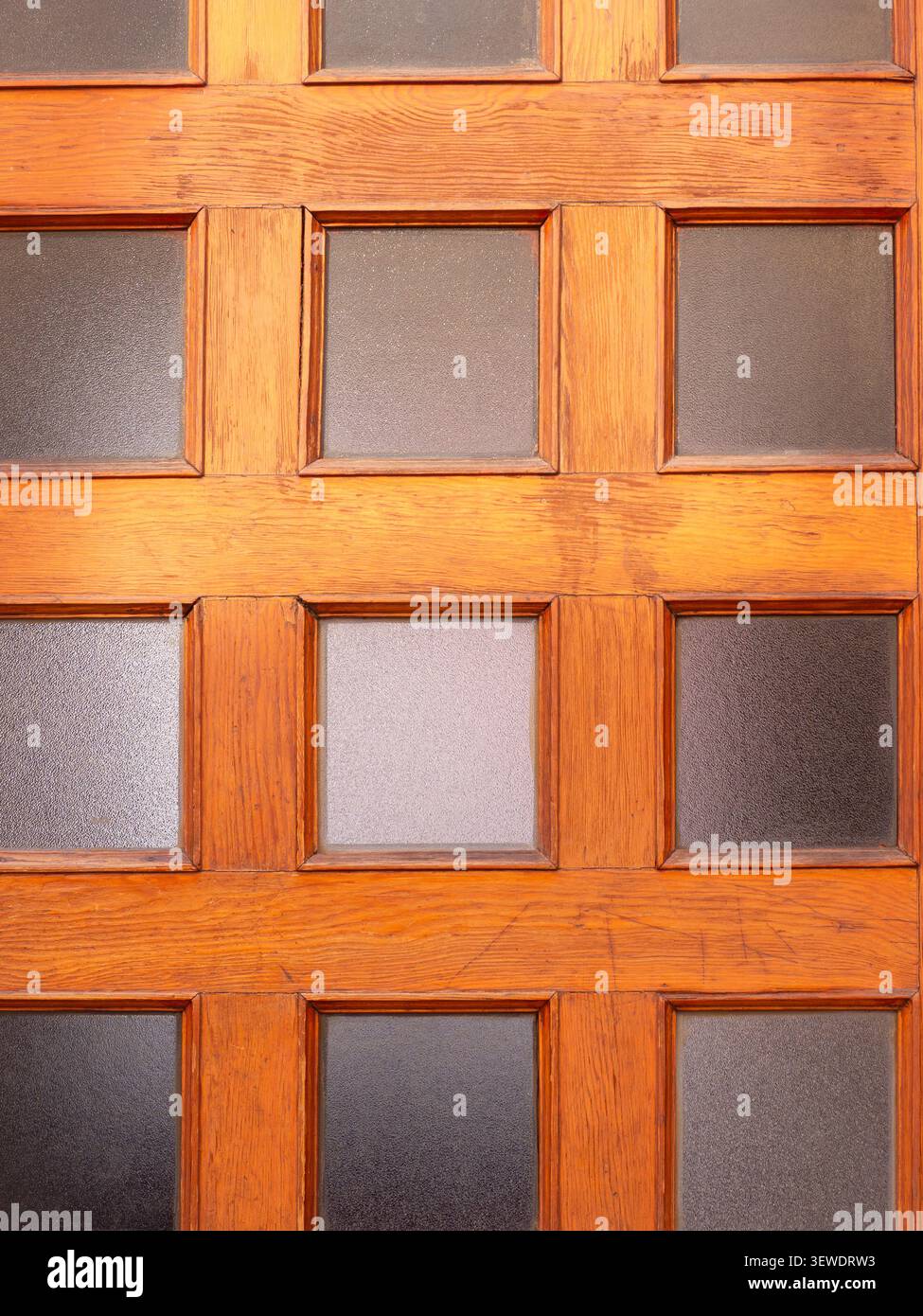 Holztür mit mehreren quadratischen mattierten Glaspaneelen, die ein geometrisches Muster erzeugen Stockfoto