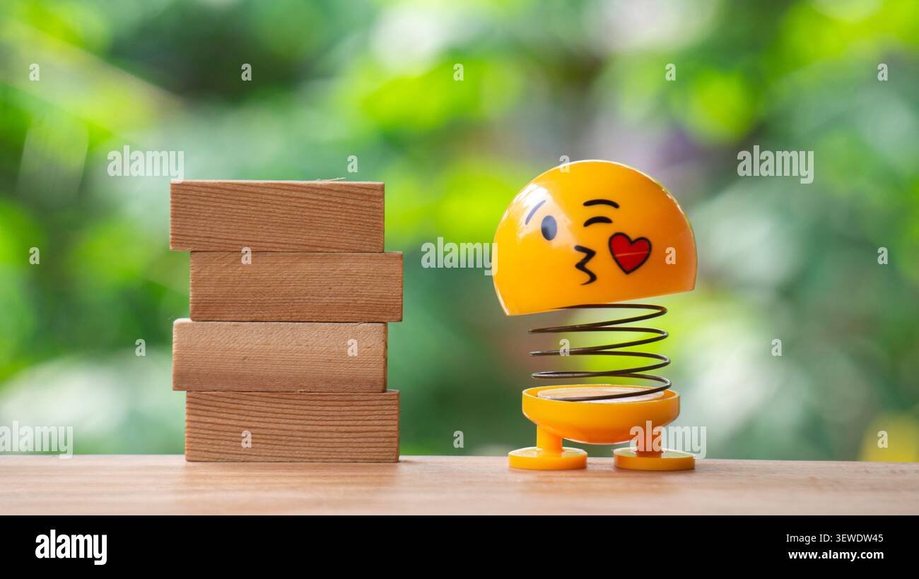 Küssendes Emoji-Spielzeug neben Holzblöcken auf Naturhintergrund Stockfoto