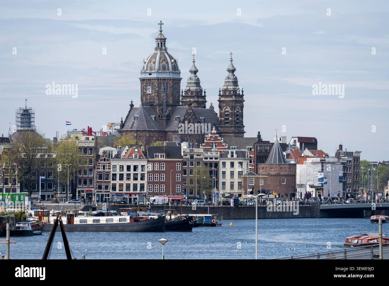 Amsterdam, Niederlande - 15. April 25: Die Skyline von Amsterdam mit der Basilika des Heiligen Nikolaus und historischen Kanalhäusern entlang der Uferpromenade. Stockfoto