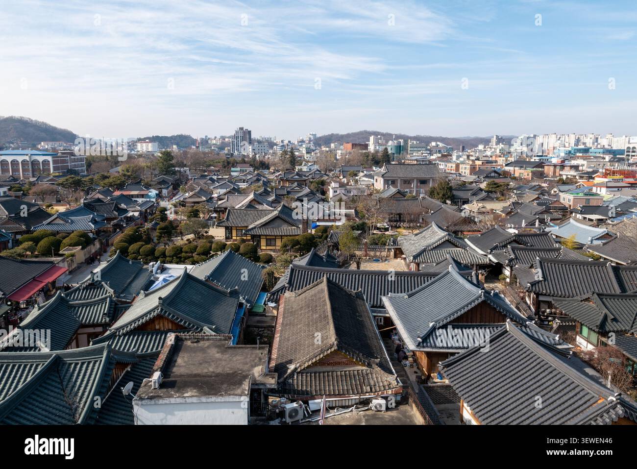 Erhöhte Ansicht über die traditionellen Ziegeldächer des Jeonju Hanok Village mit der modernen Stadtsilhouette unter einem blauen Himmel, Südkorea. Stockfoto