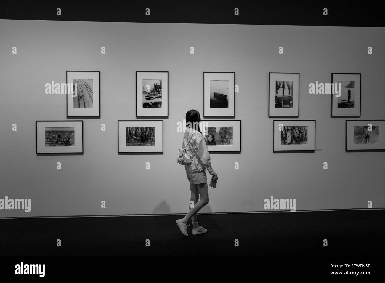 Eine junge Frau von hinten in einer Monochrom-Kunstgalerie, die sich schwarze und weiße Fotografien an der Wand ansieht. Stockfoto